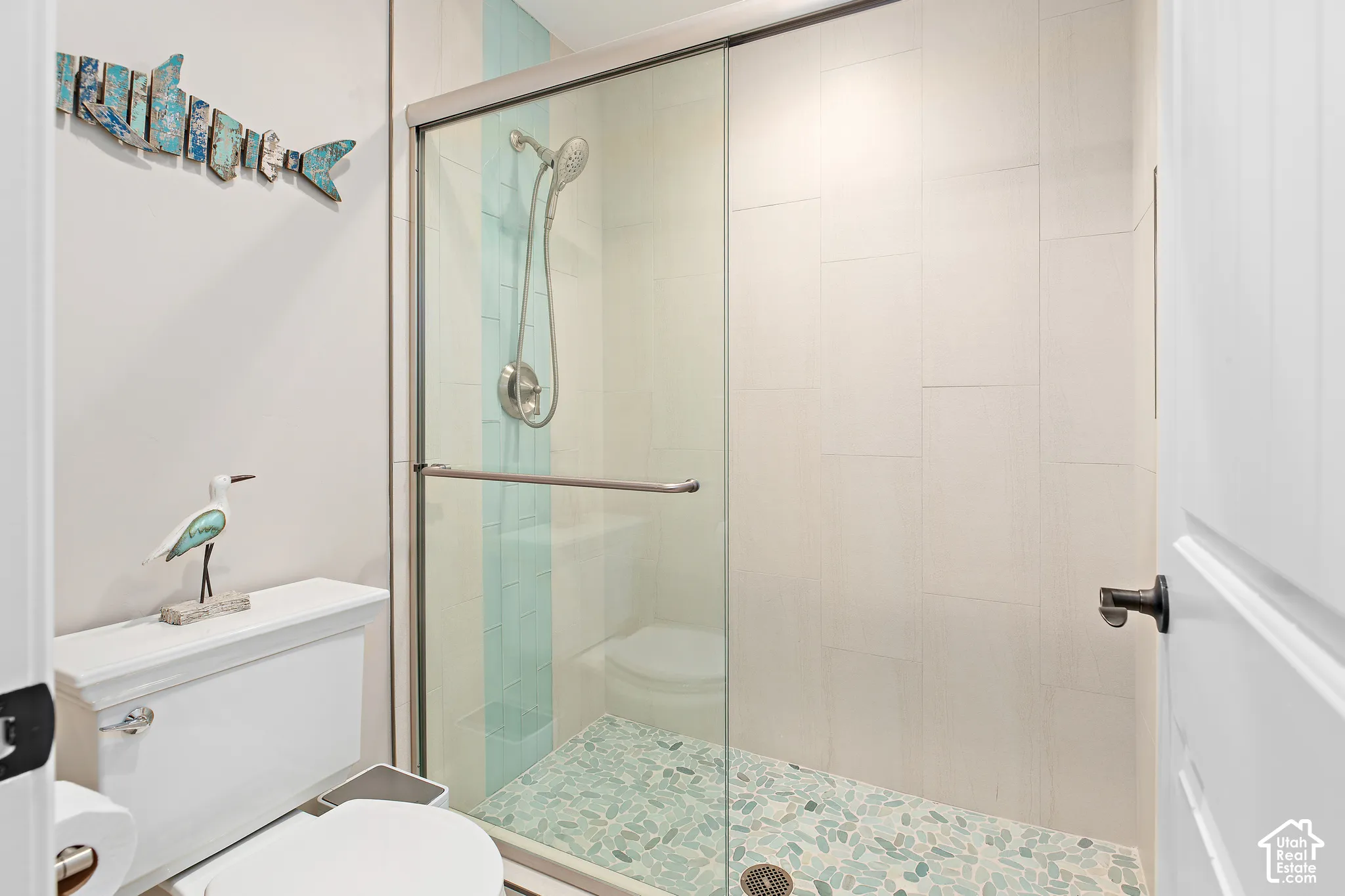 Glass-enclosed shower with pebble-style flooring and a light-colored tile surround featuring a vertical accent stripe