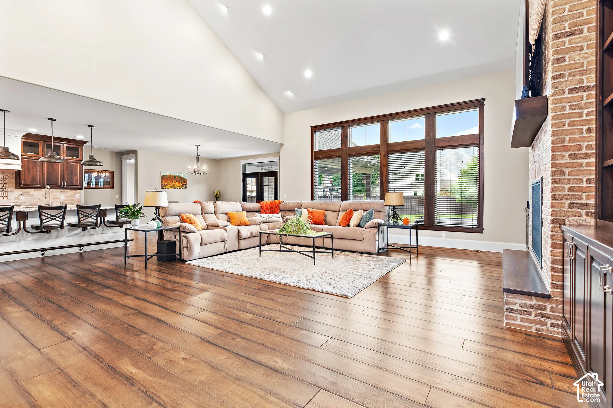 Vaulted ceiling with recessed lighting, wood-finish flooring, large multi-pane windows, brick-faced fireplace with wood mantel, and built-in cabinetry