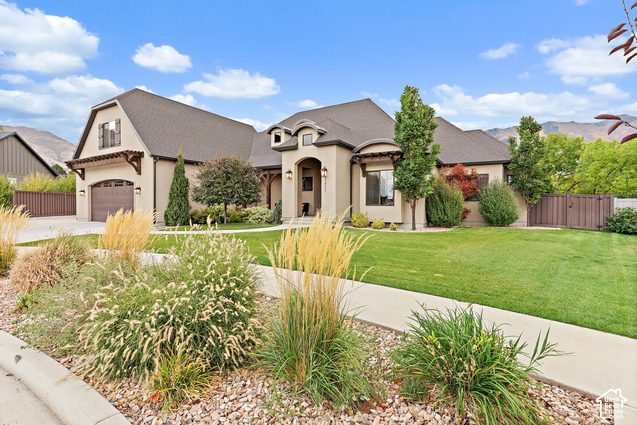 Stucco exterior with arched entry, two-car garage, and landscaped front yard featuring mature trees and shrubs