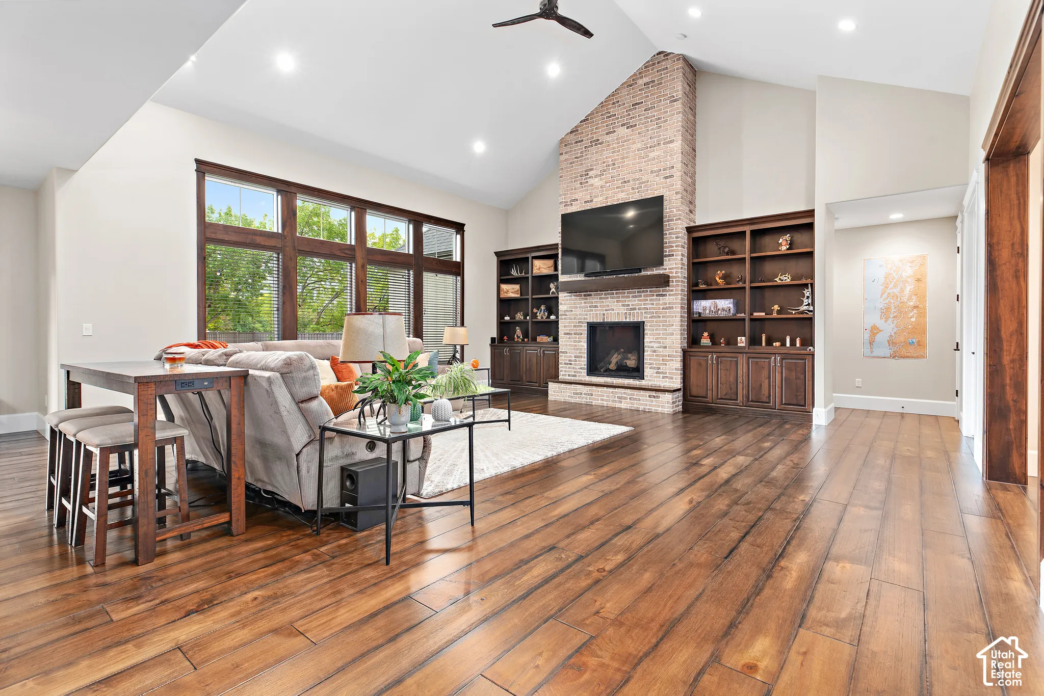 Vaulted ceilings, wood-finish flooring, full-height brick fireplace, built-in shelving, and expansive windows