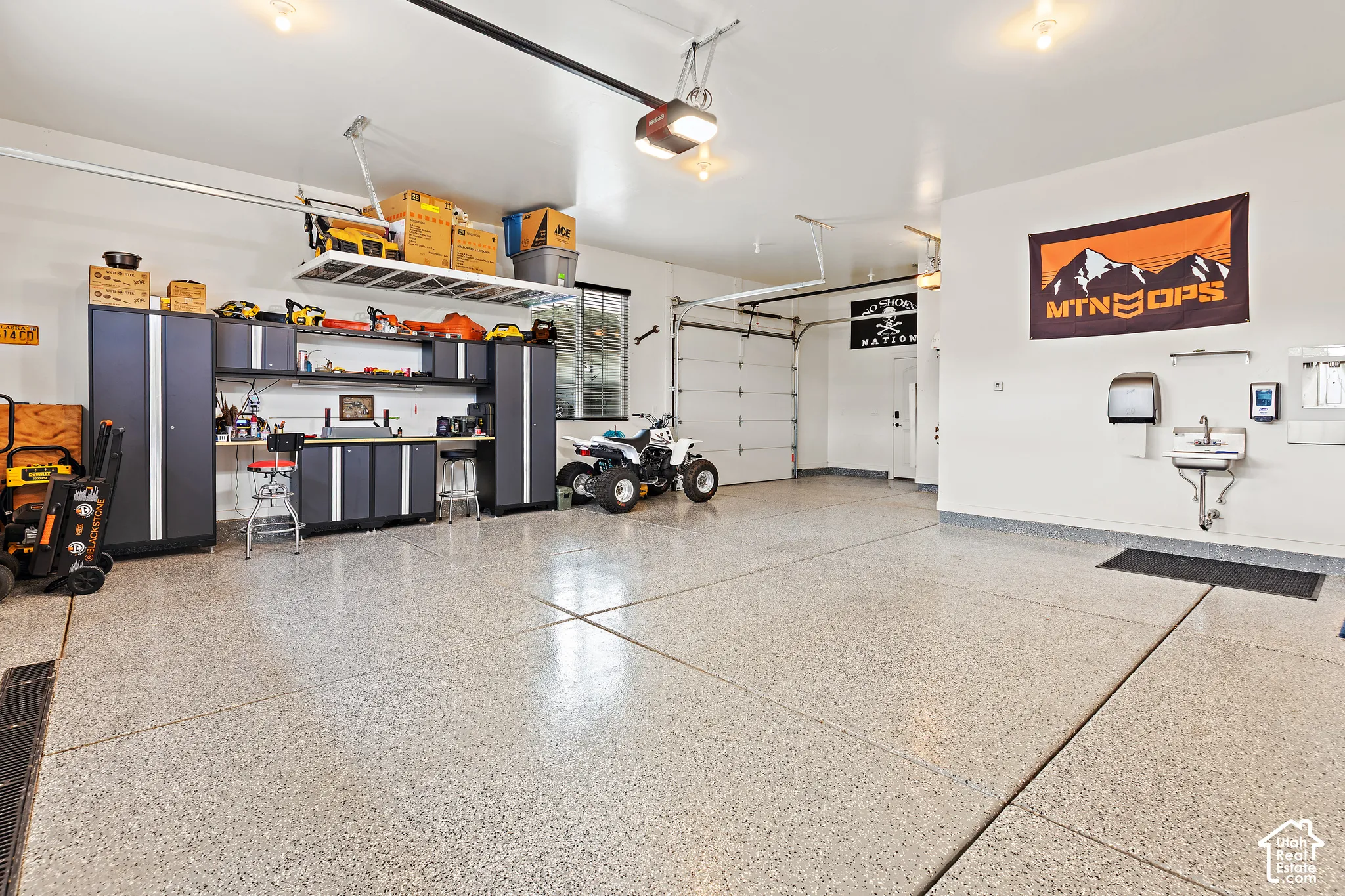 Expansive garage with durable epoxy flooring, built-in cabinetry, overhead storage, and a utility sink