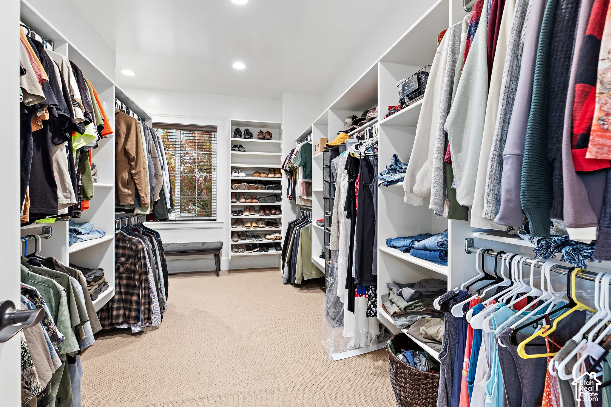 Spacious walk-in closet featuring extensive built-in shelving, multiple hanging rods, recessed lighting, and a window with blinds