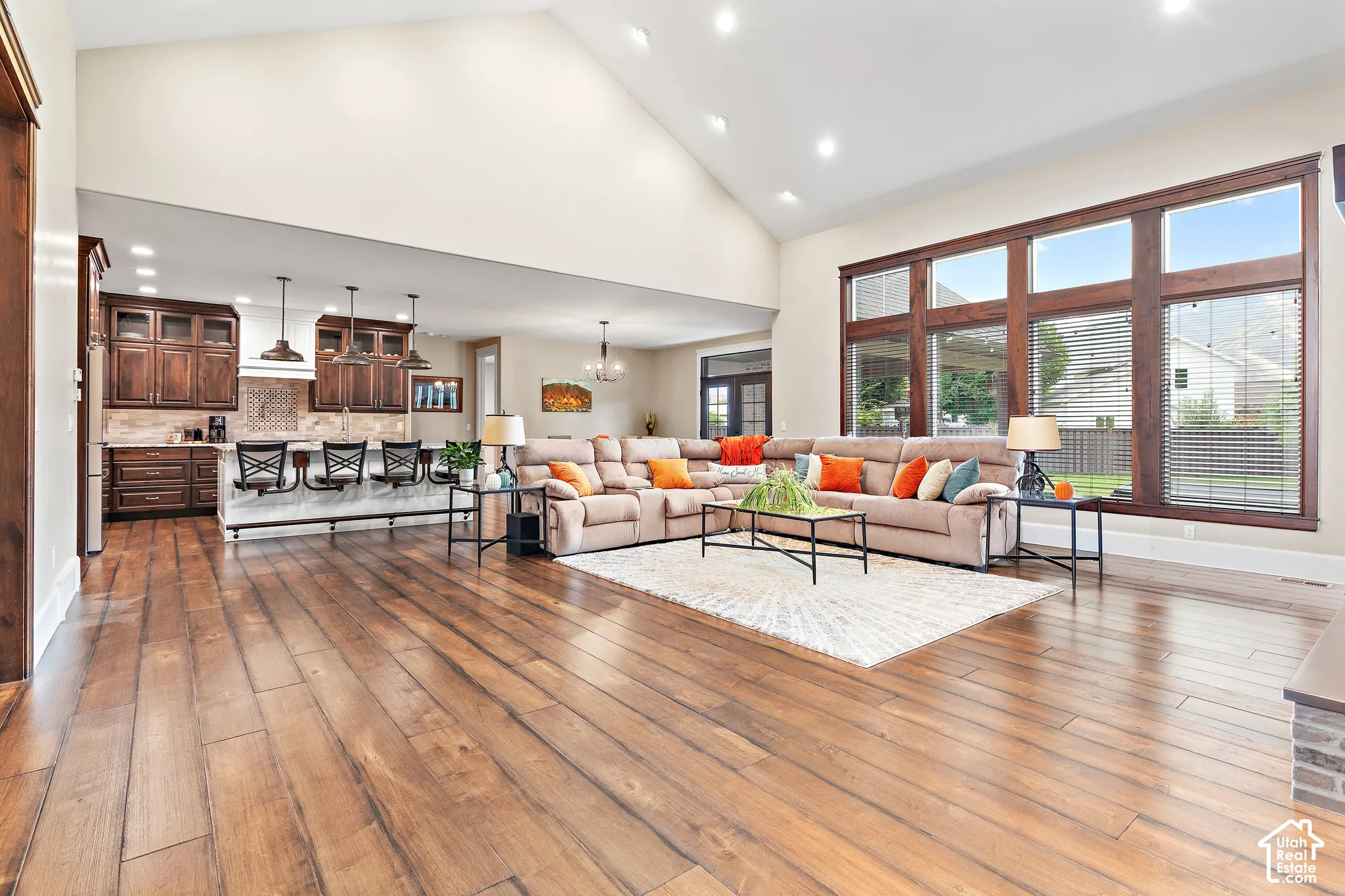 Vaulted ceiling with recessed lighting, rich wood-finish flooring, custom wood cabinetry, a central island with integrated seating, and expansive windows