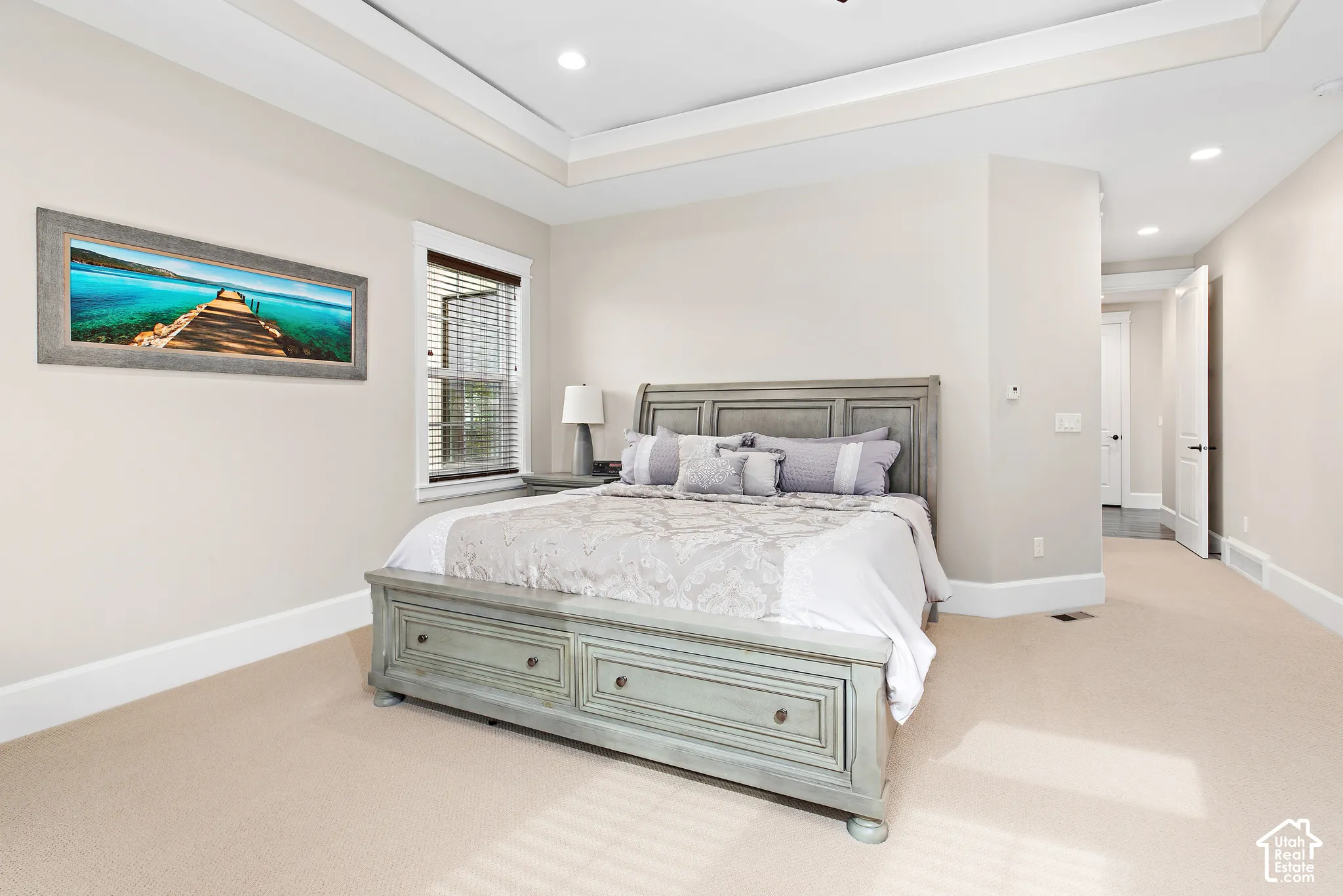 Tray ceiling with recessed lighting, light neutral-toned walls, wall-to-wall carpeting, and a window with blinds