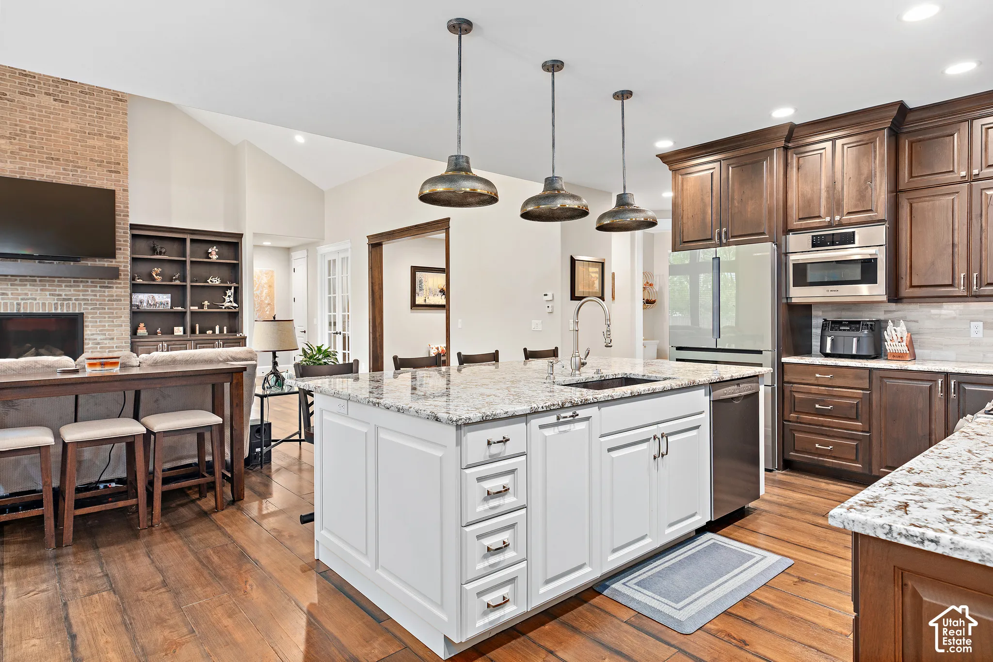 White kitchen island with a built-in sink, stainless steel appliances, wood-finish flooring, and vaulted ceilings