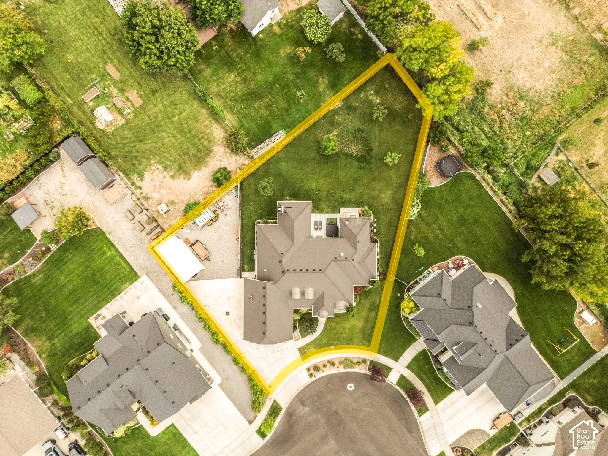 Expansive property featuring a large residence with a multi-gabled roofline, substantial green space with mature trees, and a paved driveway leading to a cul-de-sac
