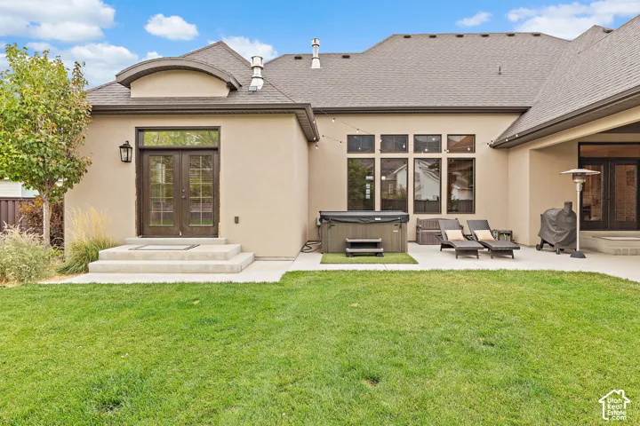 Expansive manicured lawn with a stucco exterior, double French doors, large windows, and an outdoor spa