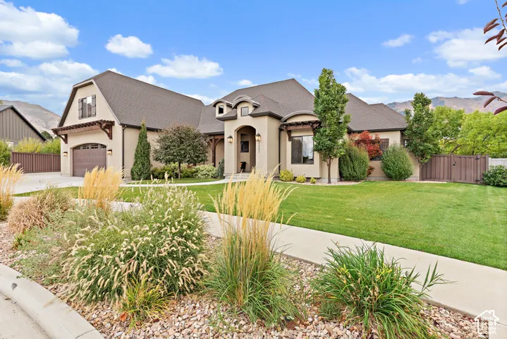 Stucco exterior with arched entry, two-car garage, and landscaped front yard featuring mature trees and shrubs