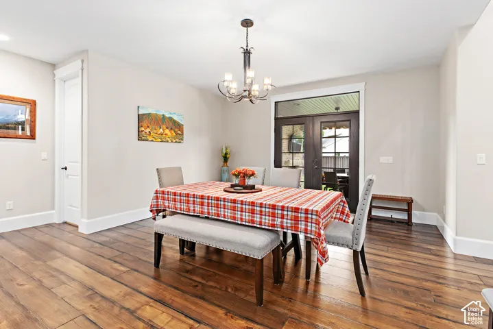 Hardwood-style flooring with a chandelier, light-toned walls, and dark-framed double doors