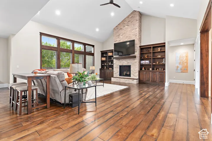 Vaulted ceilings, wood-finish flooring, full-height brick fireplace, built-in shelving, and expansive windows