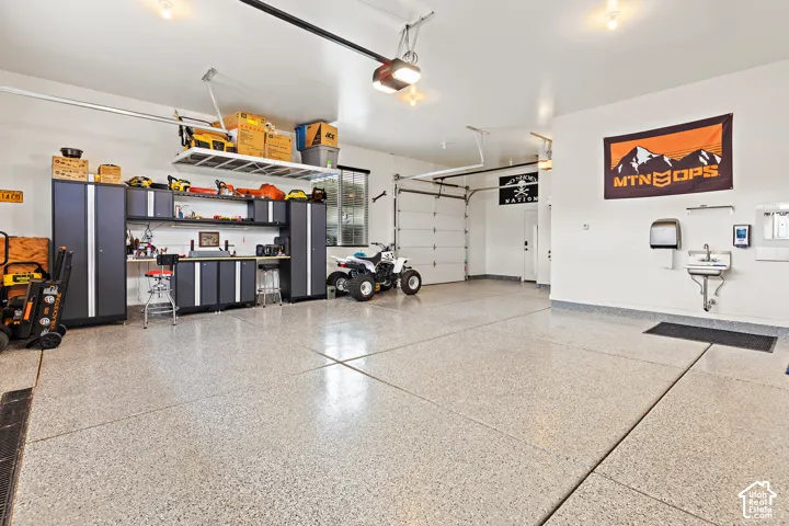 Expansive garage with durable epoxy flooring, built-in cabinetry, overhead storage, and a utility sink