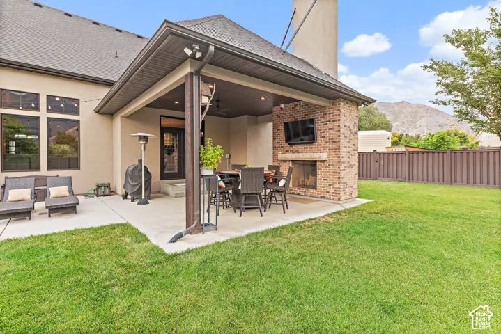 Expansive concrete patio featuring a covered outdoor living area with a brick fireplace, built-in outdoor television, and mountain backdrop