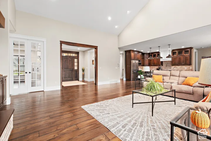 Vaulted ceiling with recessed lighting, dark wood-finish flooring, white French doors, dark wood-finish entryway, and a full kitchen with stainless steel appliances