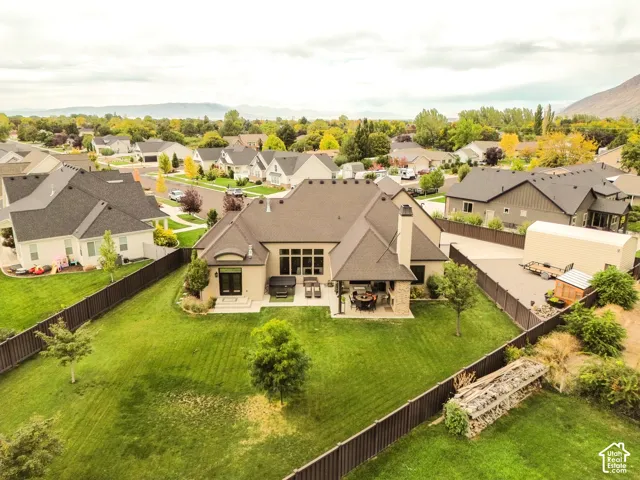 Expansive rear yard featuring a manicured lawn and mature trees, covered patio, outdoor dining area, and a private fence