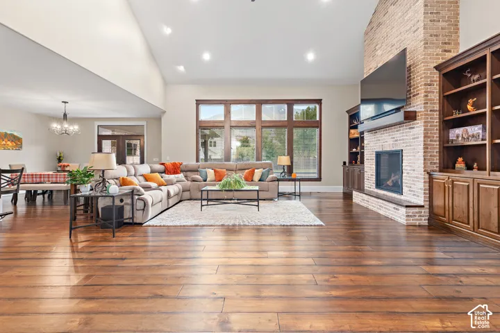 High vaulted ceiling, wood-finish flooring, brick-clad fireplace, built-in shelving, and large multi-pane windows