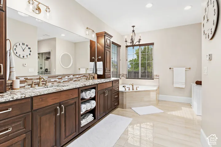 Double vanity with granite countertop and integrated sinks, wood-finish cabinetry, built-in soaking tub with tiled surround, and polished tile flooring