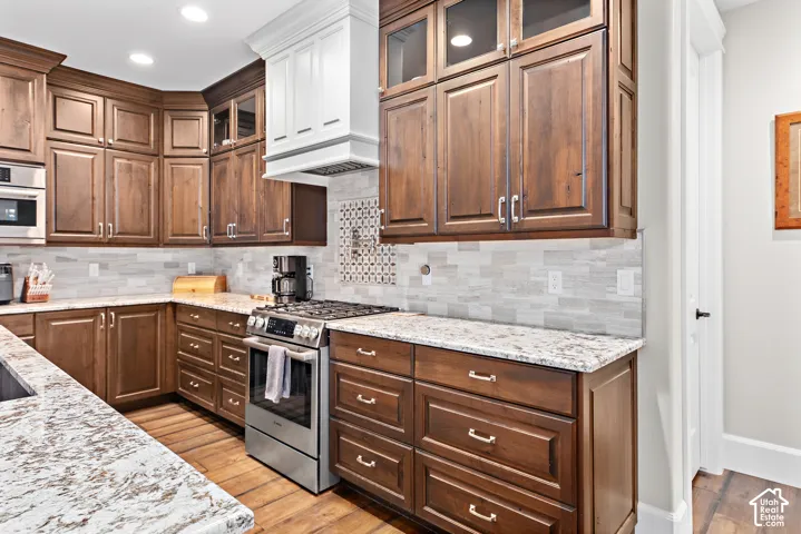 Rich wood-finish cabinetry with crown molding, light-toned stone countertops, stainless steel appliances, and a tiled backsplash