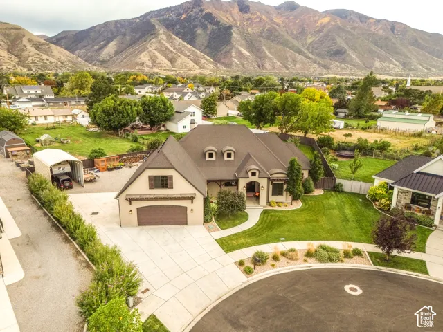 Stucco exterior with stone accents, mature landscaping, paved driveway, two-car garage, and a peaked roofline