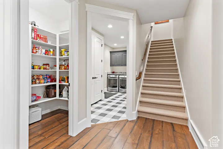 Walk-in pantry with extensive built-in shelving, wood-finish flooring, carpeted staircase, and tiled floor entry to a utility area