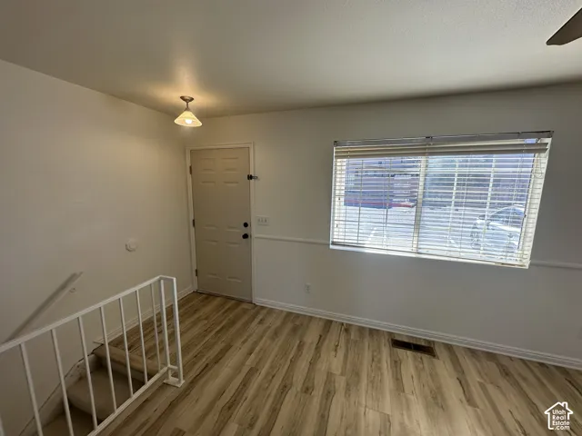 Wood-finish flooring, white painted walls, ceiling-mounted light fixture, white interior door, and a horizontal window with blinds