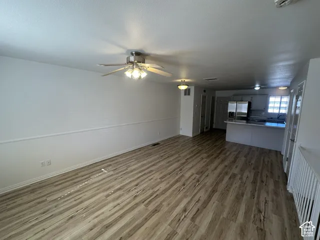 Wood-finish flooring throughout, ceiling fan with integrated lighting, chair rail molding, kitchen island with countertop, and stainless steel refrigerator