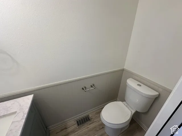 Vanity with a marble-finish countertop, white ceramic toilet, wood-finish flooring, and wainscoting