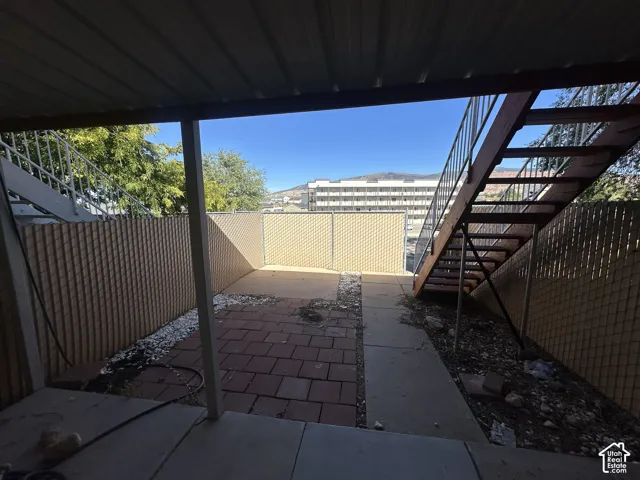 Paved patio area featuring brick pavers and concrete pathways, bordered by privacy fencing and a metal exterior staircase
