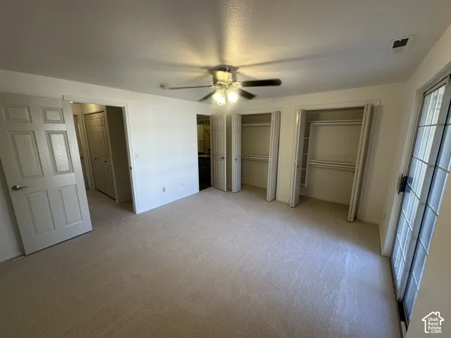 Neutral tone carpeting, dual built-in closets with shelving, ceiling fan with light fixture, and a sliding glass door
