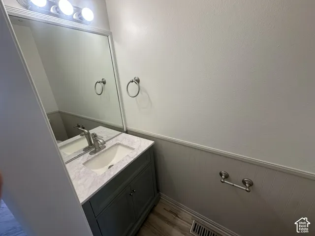 Vanity with stone-finish countertop and integrated sink, brushed nickel faucet, beadboard wainscoting, and wood-finish flooring