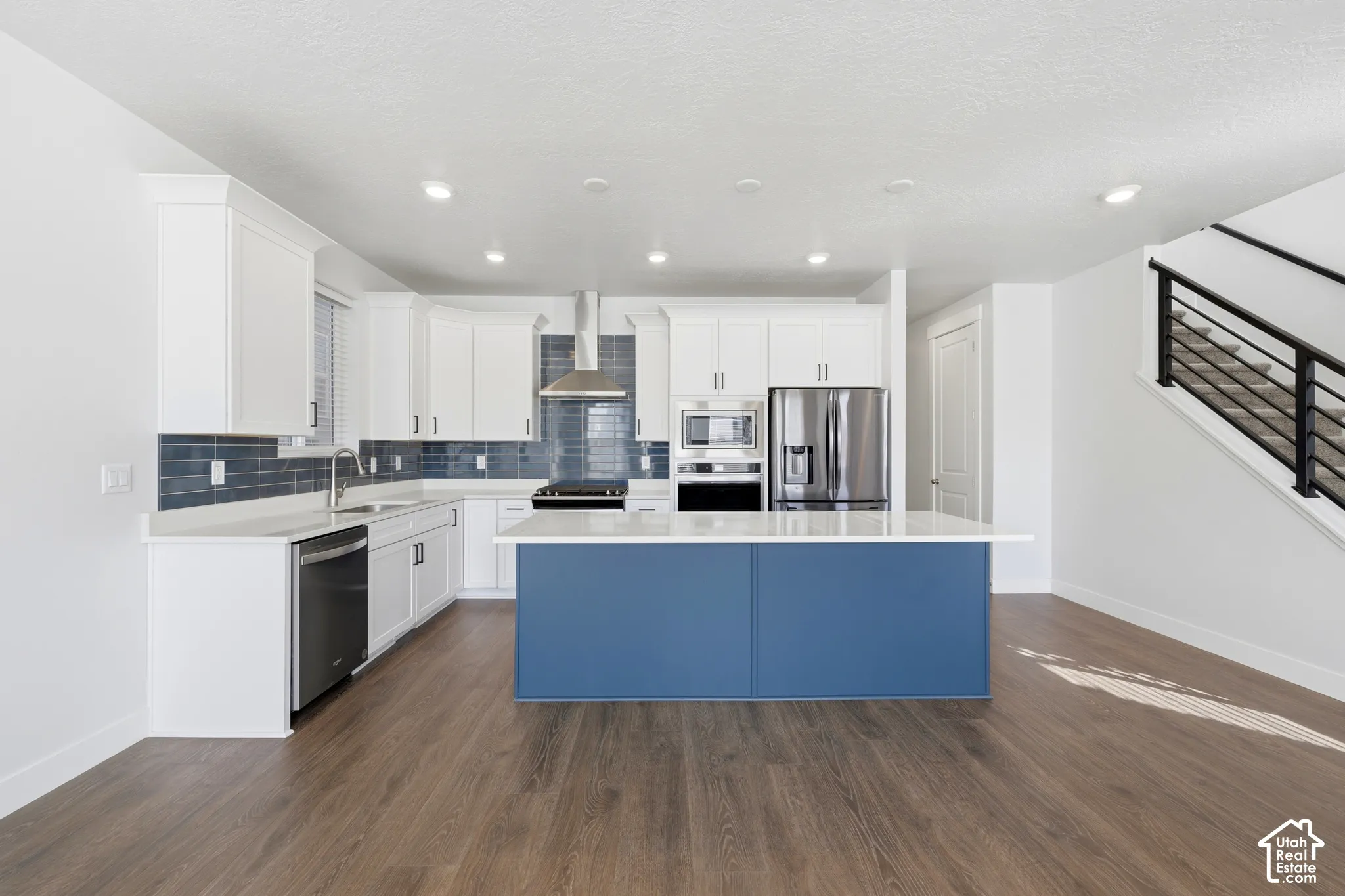 Kitchen featuring white cabinetry, stainless steel appliances, a blue center island with a white countertop, wood-finish flooring, and a subway tile backsplash