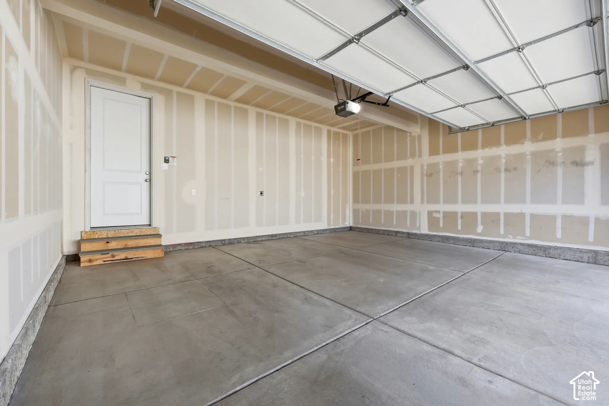 Spacious garage with a concrete floor, overhead garage door, and a white interior access door