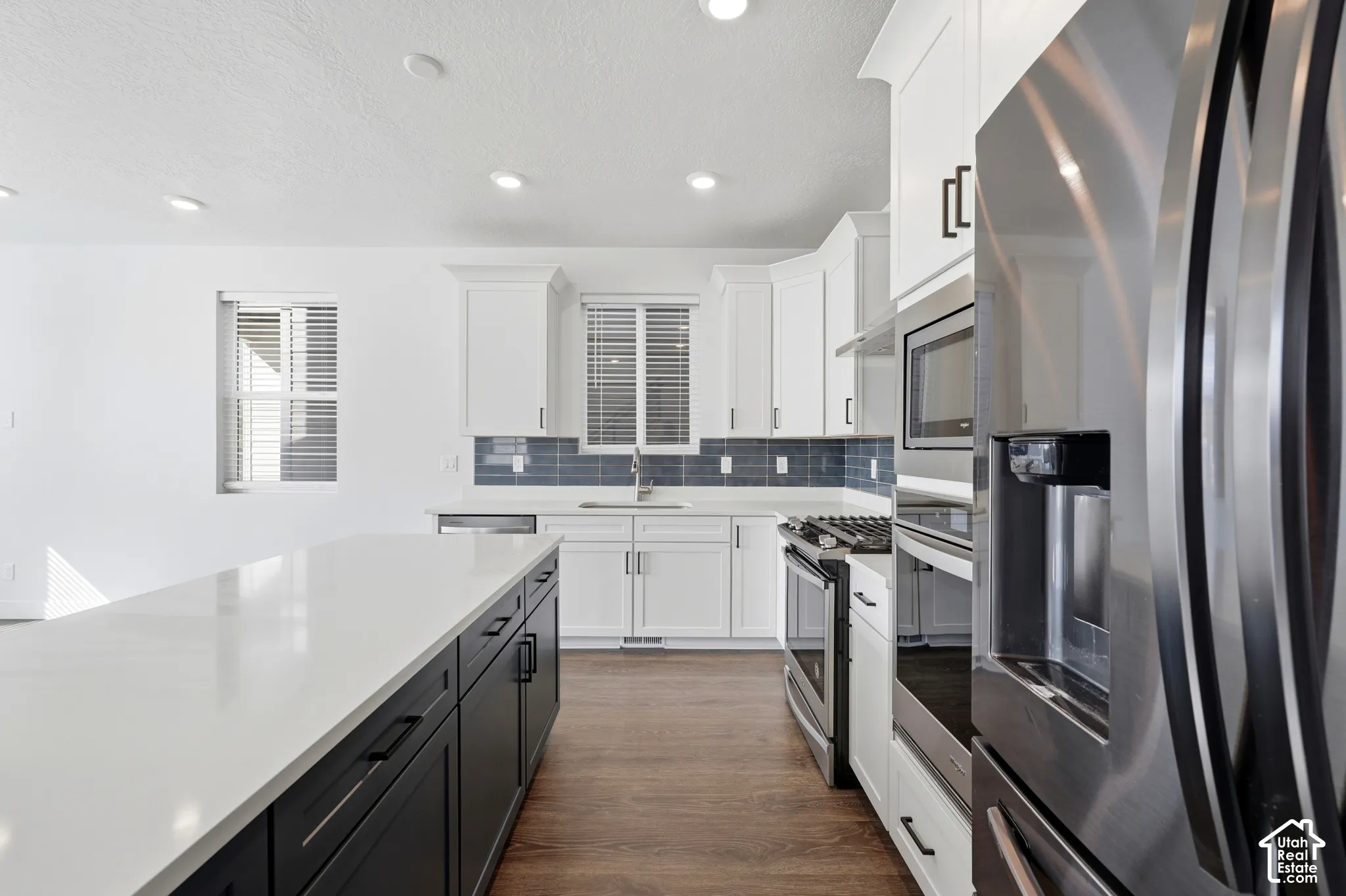 Kitchen featuring a spacious island with white countertop, dark cabinetry, and wood-finish flooring