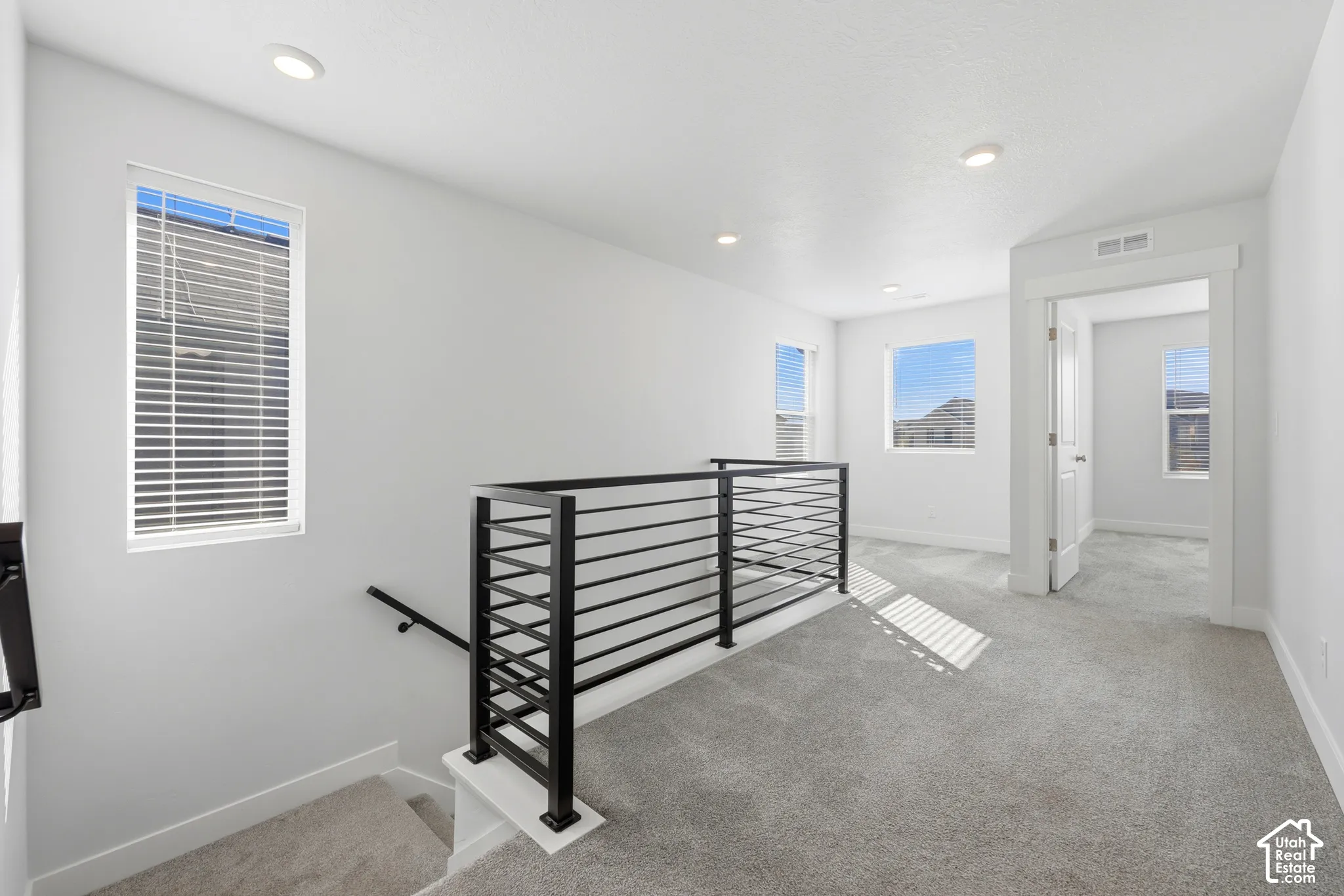 Open landing area featuring gray carpeting, recessed ceiling lighting, and multiple windows with blinds