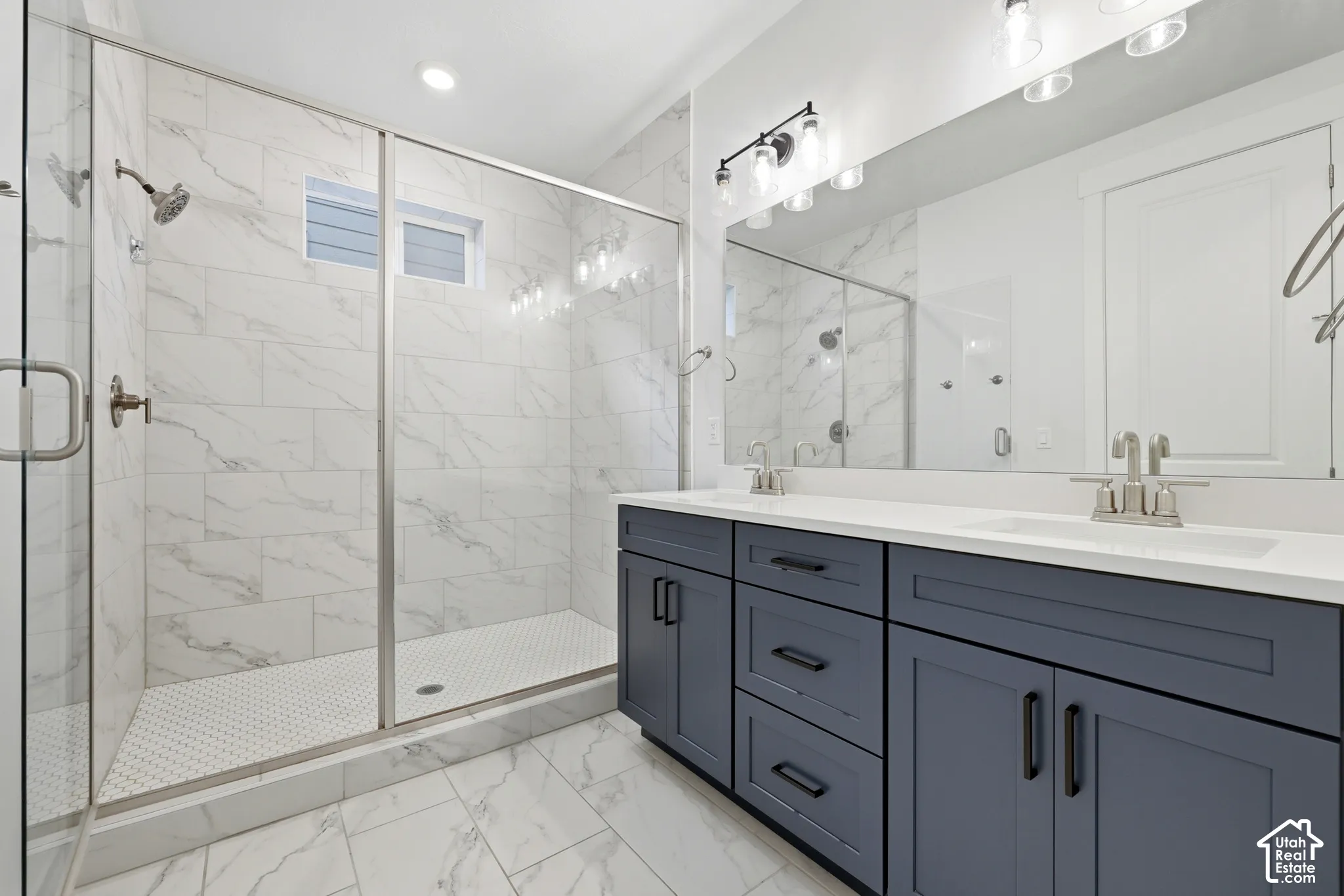 Double vanity with white countertop, chrome faucets, and dark blue cabinetry