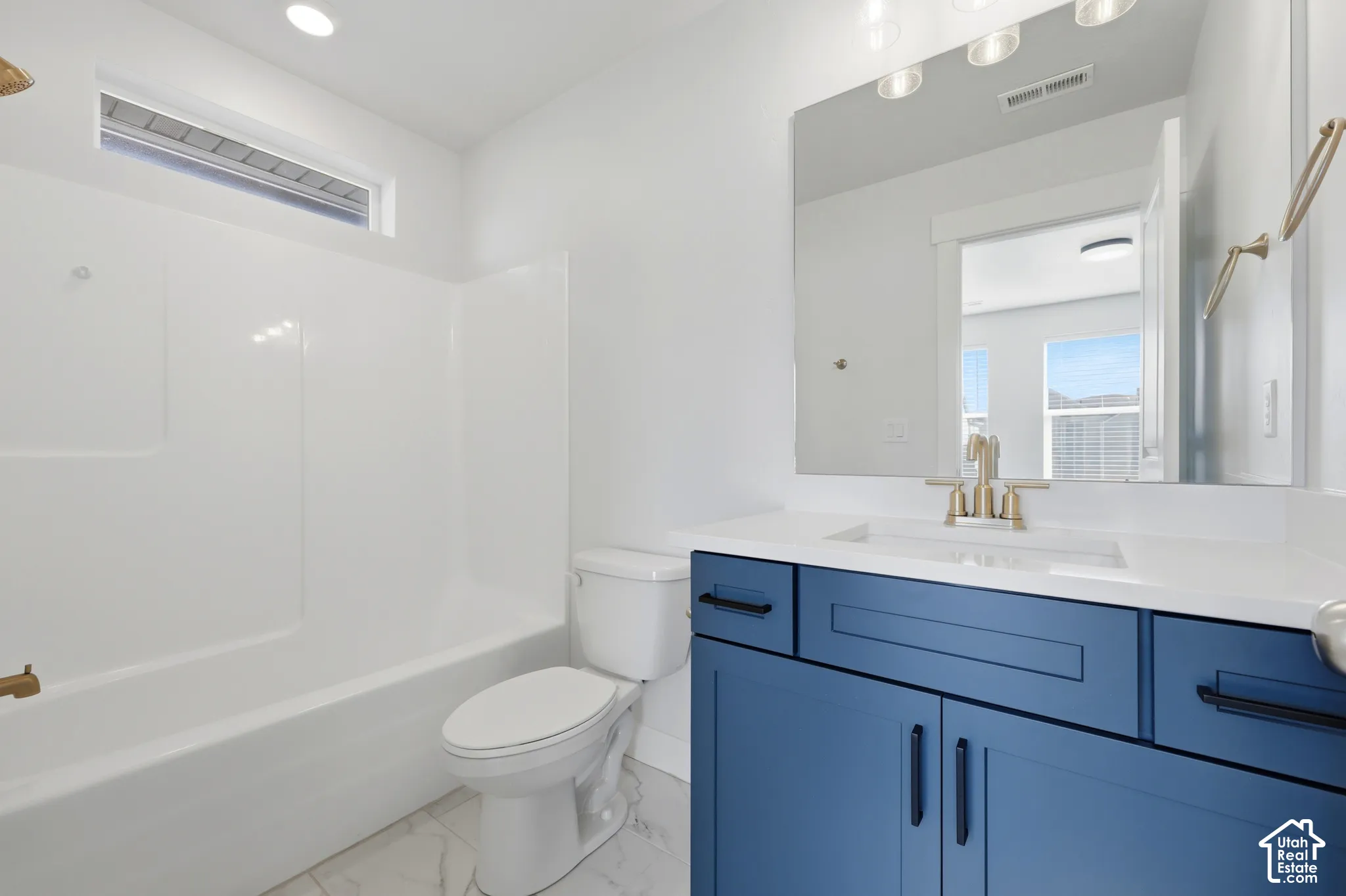 Full bathroom featuring a white tub/shower combination, white toilet, and a vanity with a white countertop and blue cabinetry