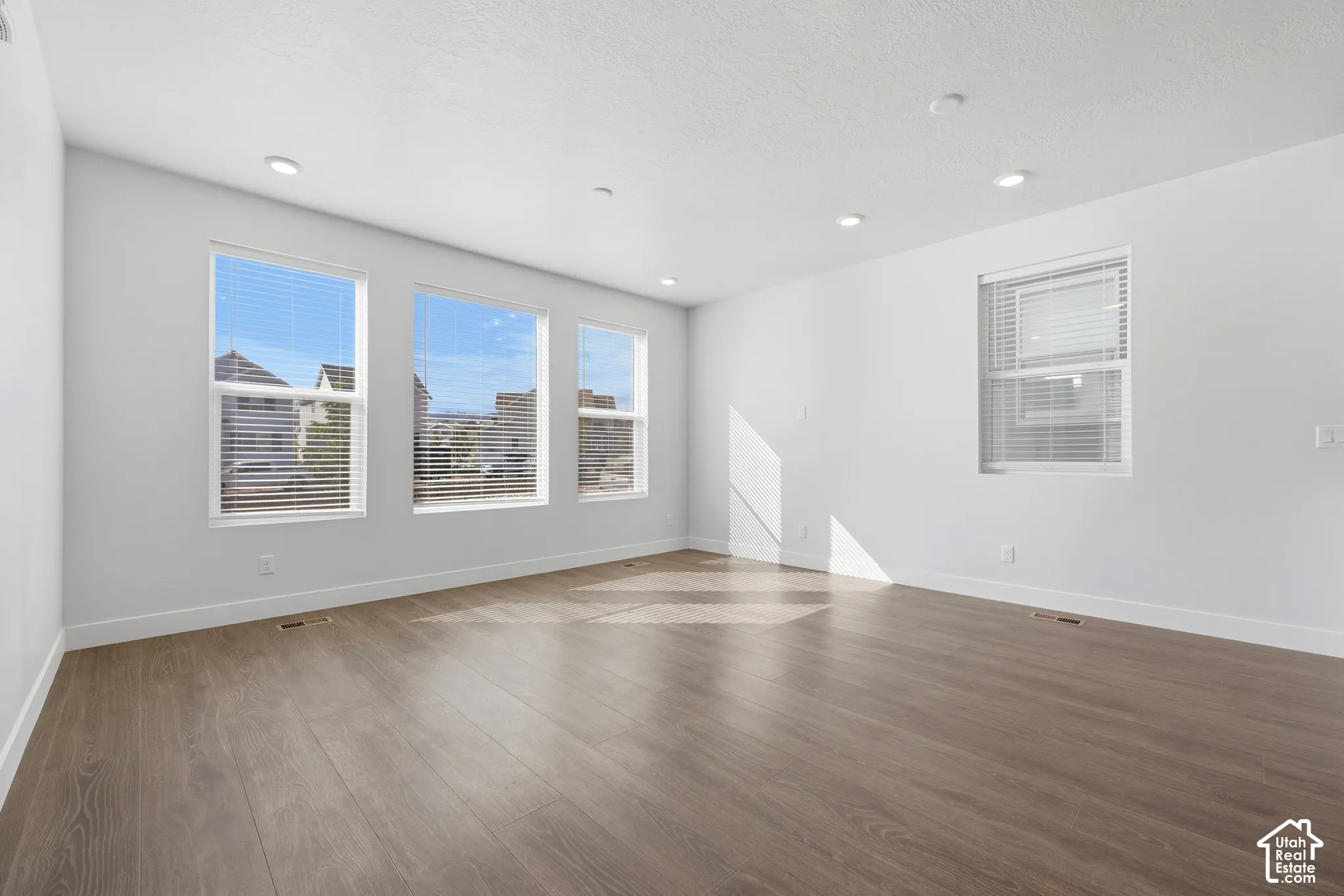 Wood-finish flooring, white walls, multiple windows, recessed lighting, and window blinds