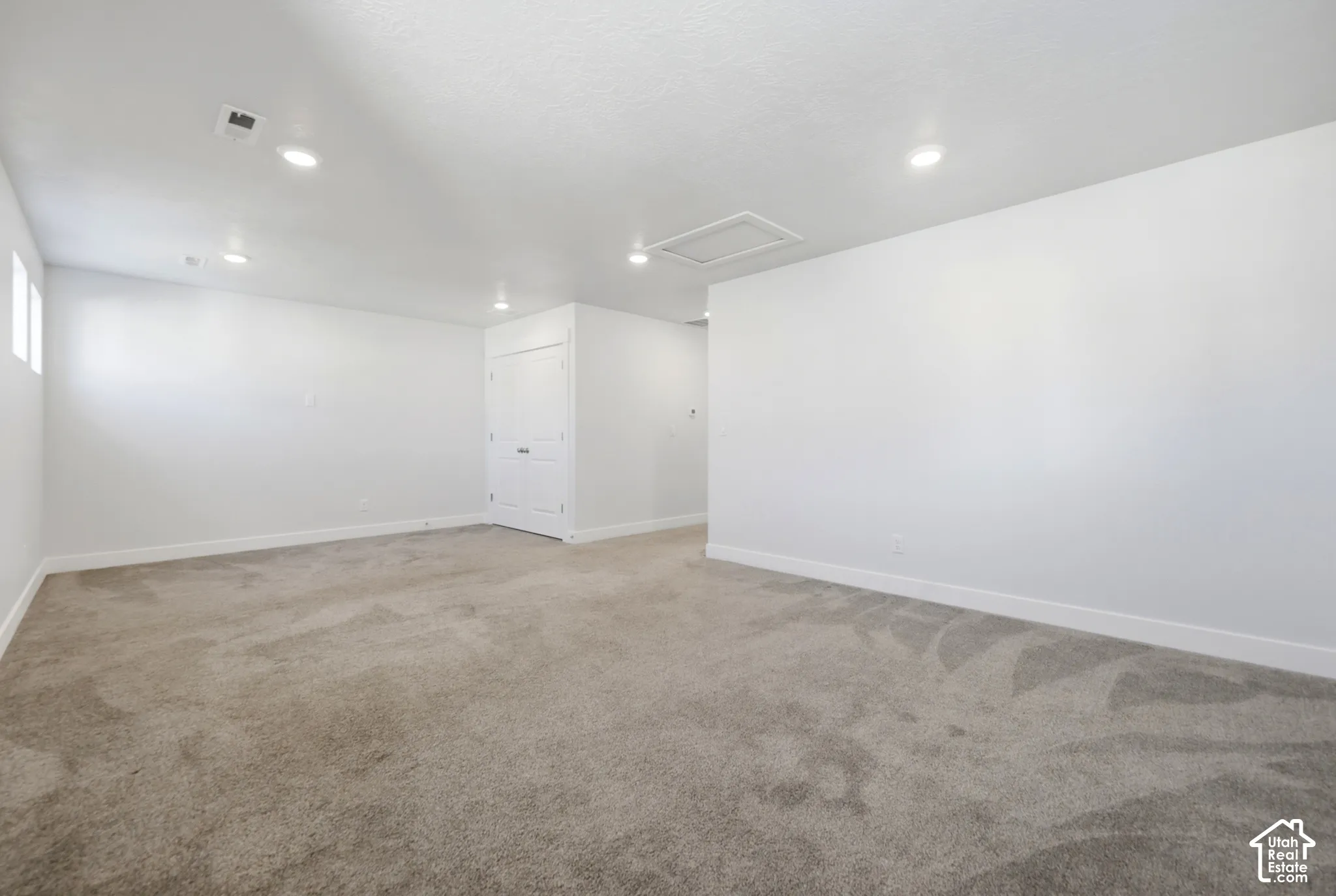 Spacious room featuring neutral carpet flooring, recessed lighting, white walls, and a white interior door