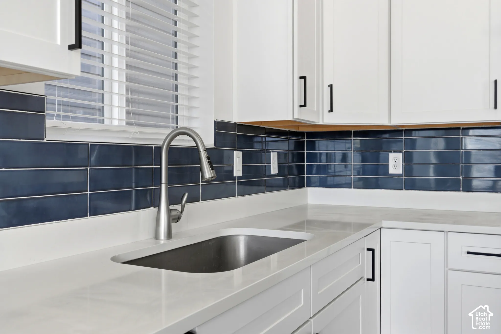 White cabinetry with matte black hardware, light-toned countertops, and a deep blue subway tile backsplash
