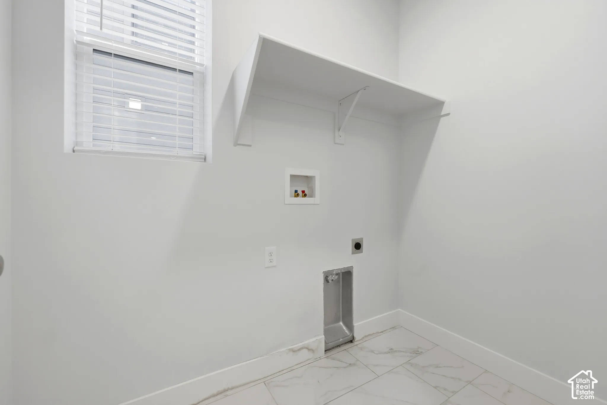 White interior walls, overhead shelving, window with blinds, plumbing hookups, and large format tiled flooring