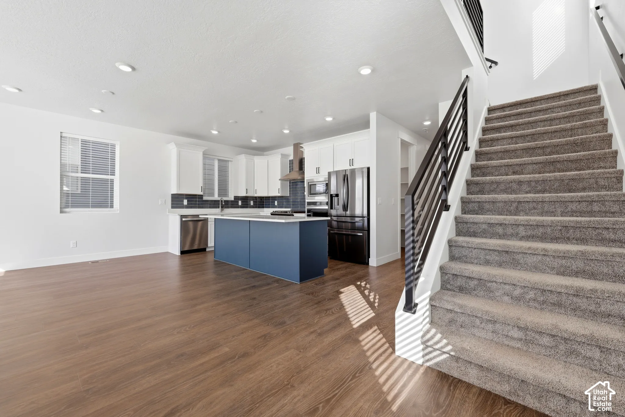 Open concept living space featuring wood-finish flooring, recessed lighting, and a modern kitchen with a blue-toned island