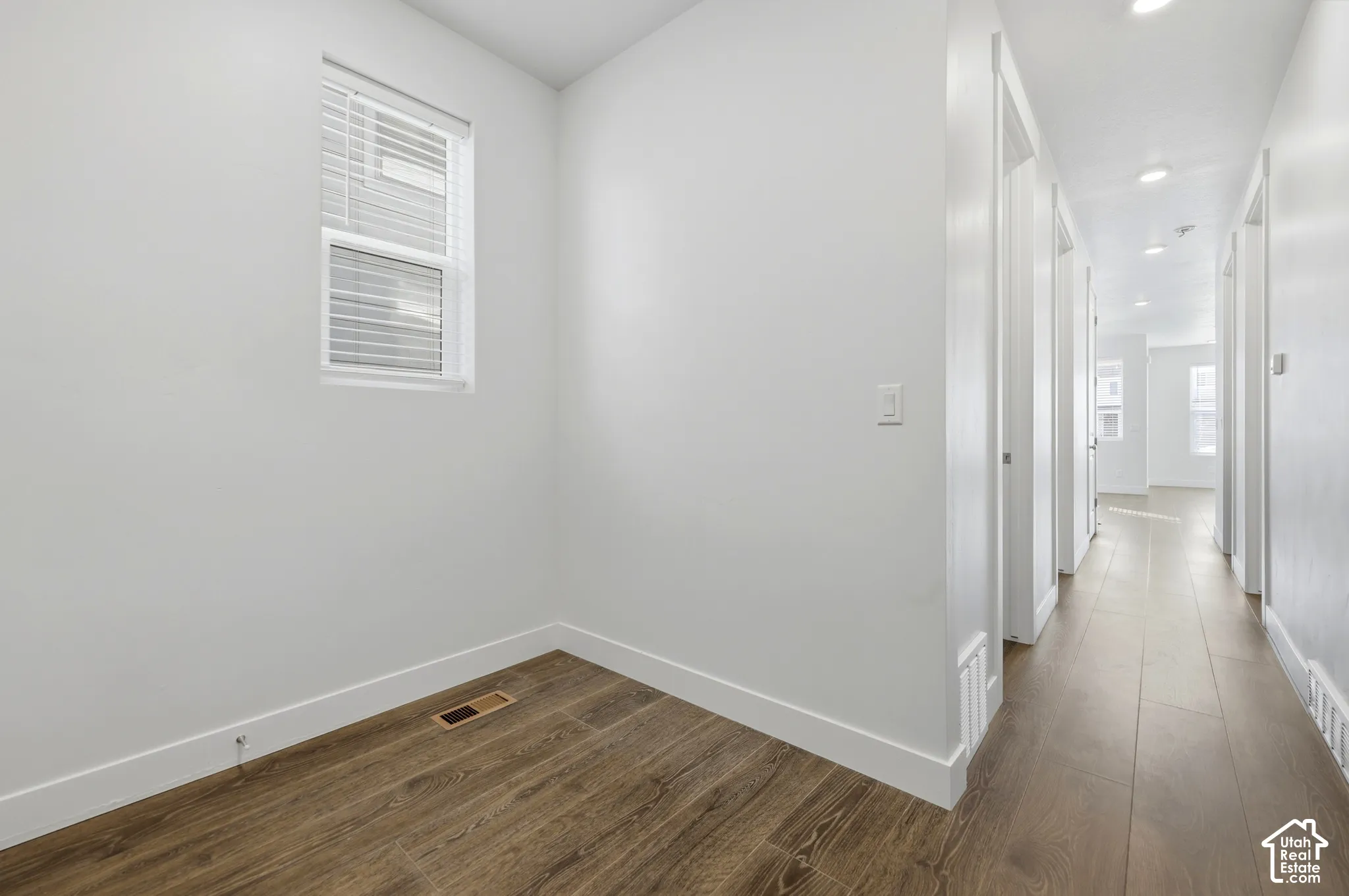 Wood-finish flooring throughout, white walls, and a recessed ceiling light in the hallway