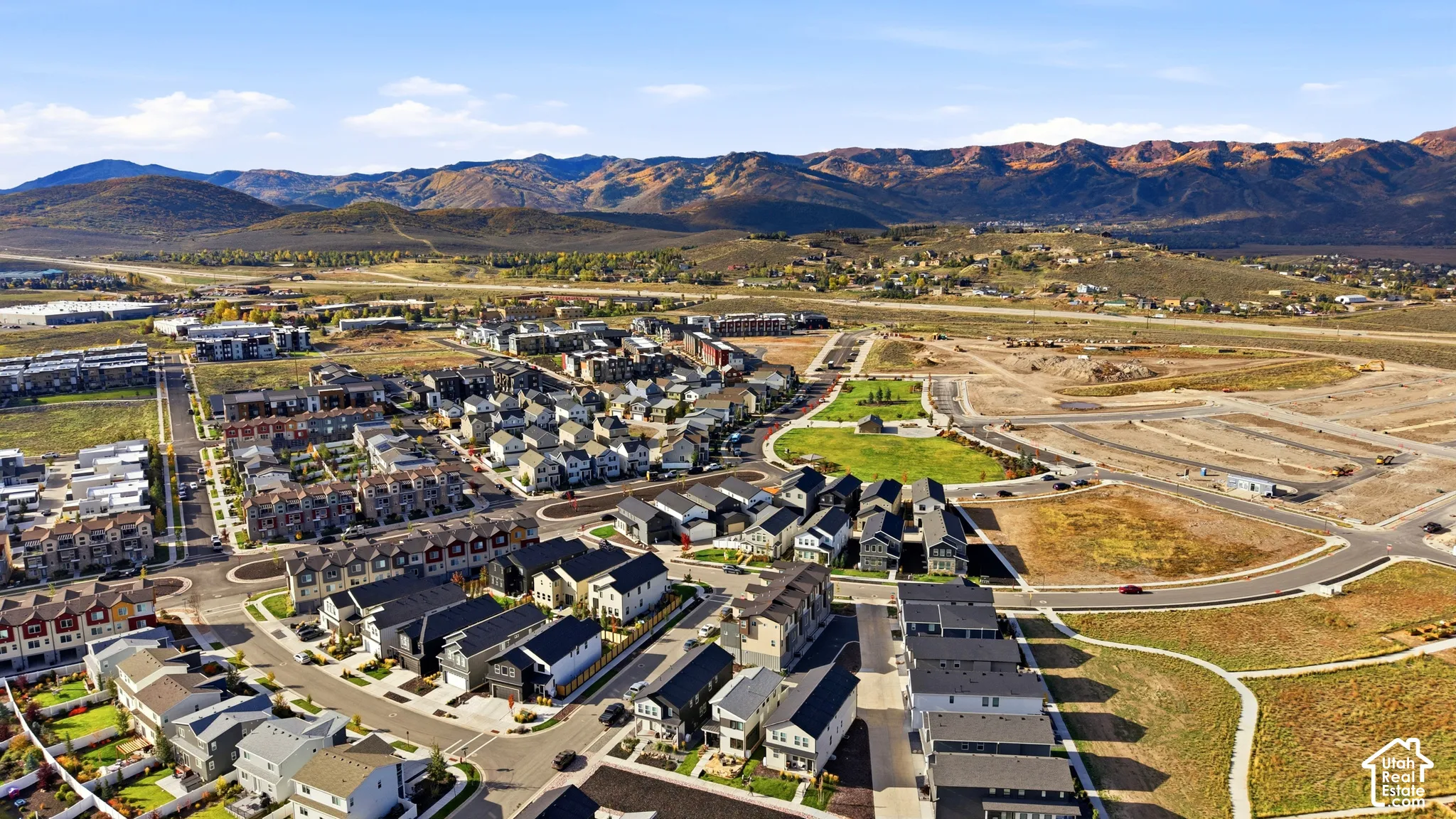 Expansive residential development with a mountain backdrop, featuring a central green space, paved roads, and organized housing clusters