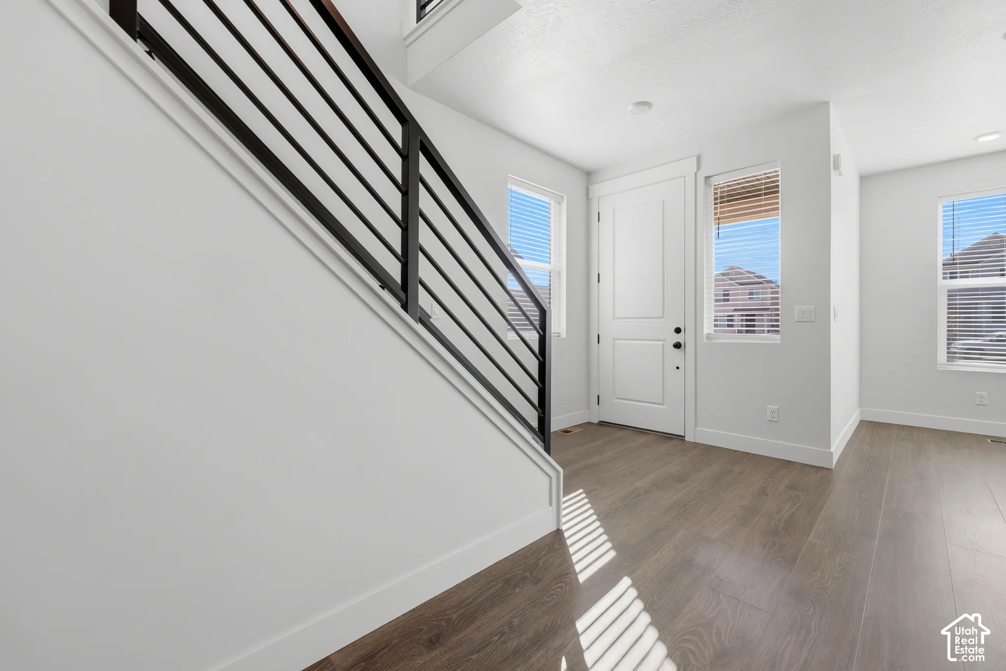 Entryway with wood-finish flooring, white walls, and a contemporary black metal staircase railing