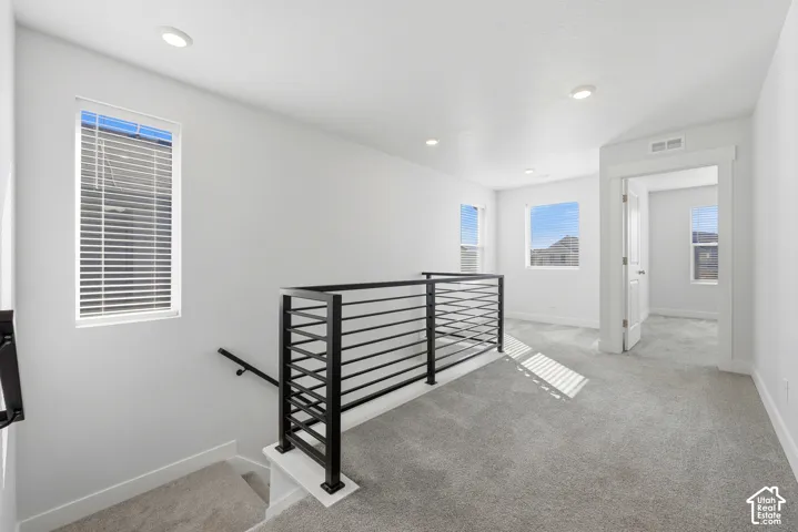 Open landing area featuring gray carpeting, recessed ceiling lighting, and multiple windows with blinds