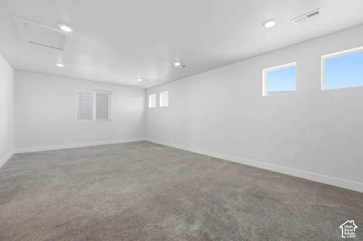 Expansive room featuring plush gray carpeting, recessed ceiling lighting, and multiple windows providing natural illumination