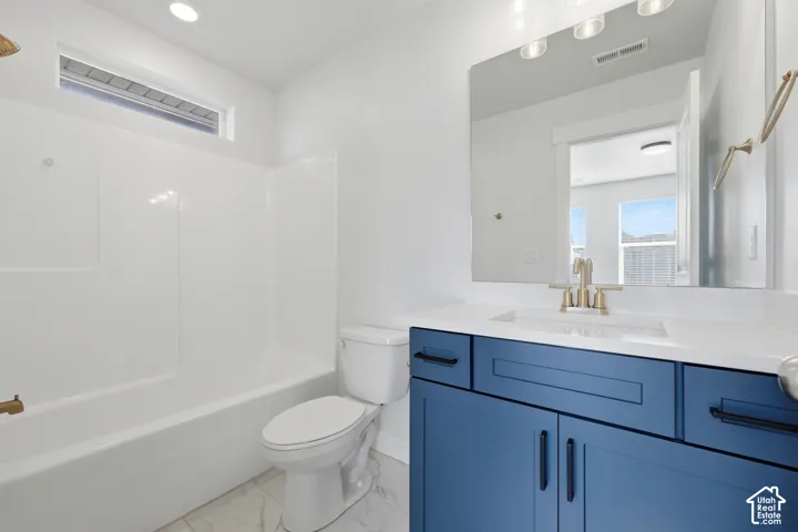 Full bathroom featuring a white tub/shower combination, white toilet, and a vanity with a white countertop and blue cabinetry