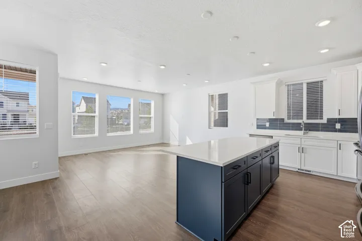 Spacious main floor with wood-finish flooring, recessed lighting, a white kitchen with a dark blue island, and a subway tile backsplash