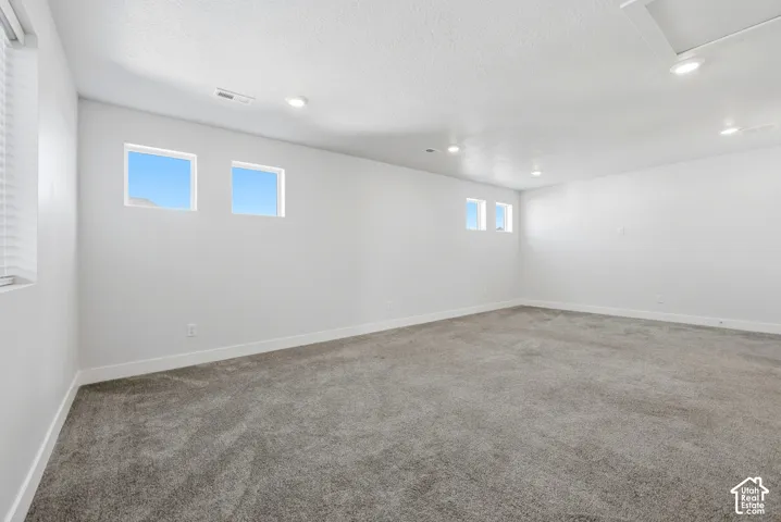 Expansive room featuring light gray carpet, white walls, multiple windows, and recessed lighting