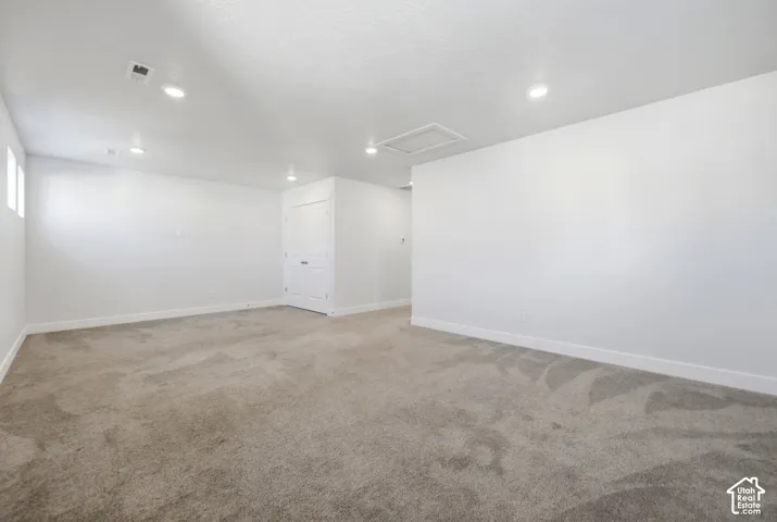 Spacious room featuring neutral carpet flooring, recessed lighting, white walls, and a white interior door