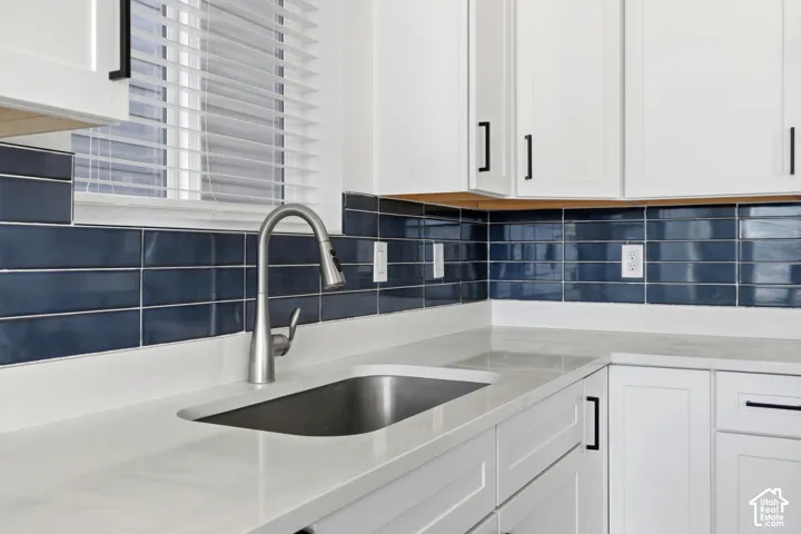 White cabinetry with matte black hardware, light-toned countertops, and a deep blue subway tile backsplash